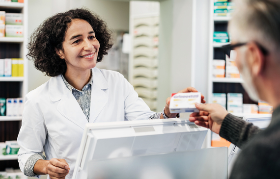 A pharmacist behind the counter, smiling while handing a customer his prescription medicine.