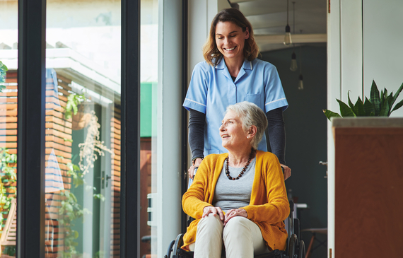 Staff working in residential aged care facility pushing an older person in a wheelchair