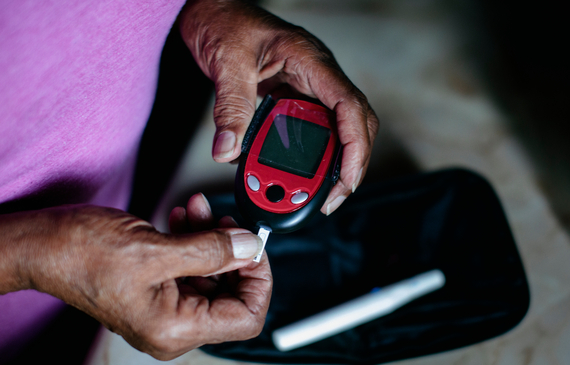 Close-up of the hands of a older woman using a blood glucose monitor and strips