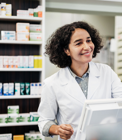A pharmacist behind the counter, smiling while handing a customer his prescription medicine.