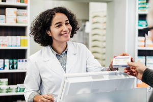 A pharmacist behind the counter, smiling while handing a customer his NDSS products.