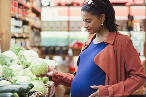 Pregnant woman shopping for cabbage in grocery store