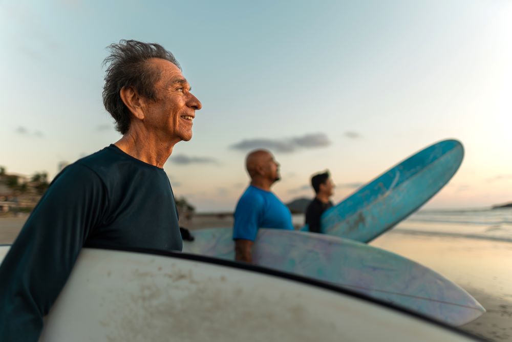 Three man standing on a beach, holding surfboards, looking out at the ocean