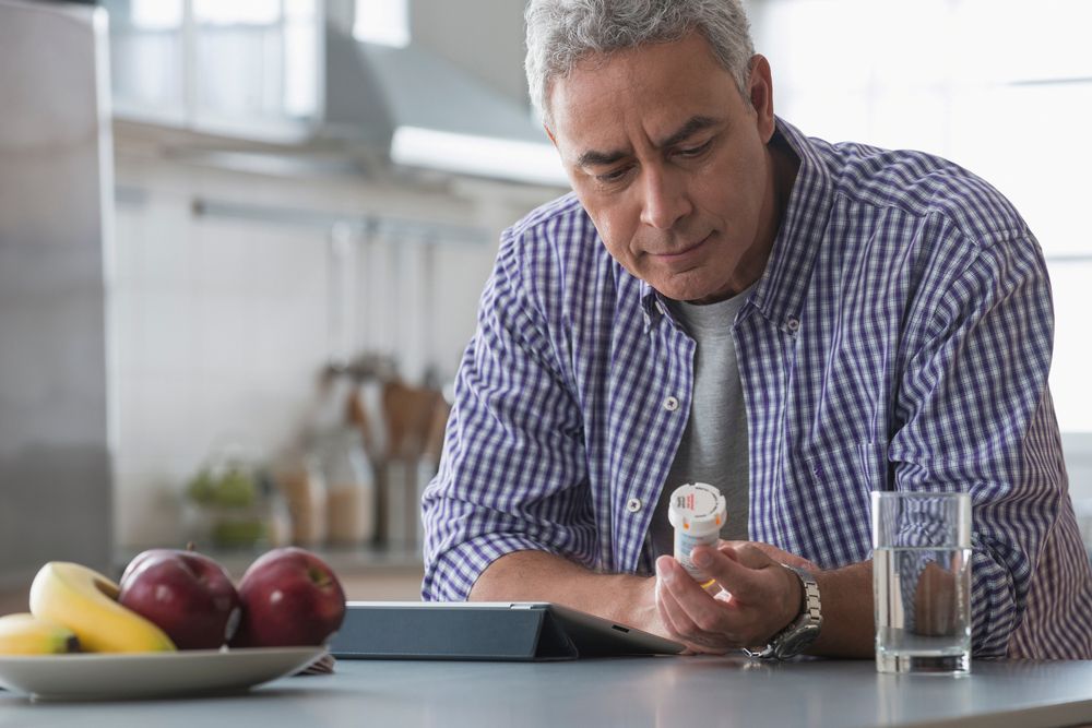 Man at kitchen bench, reading his medication capsule