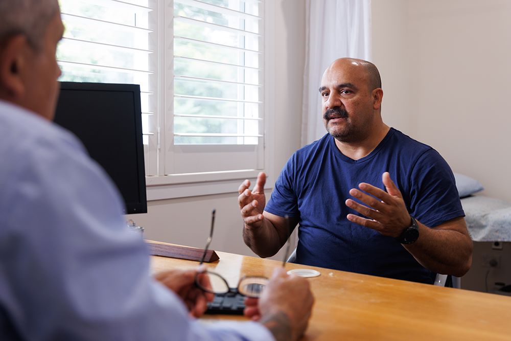 Man sitting in doctor's office, talking to doctor