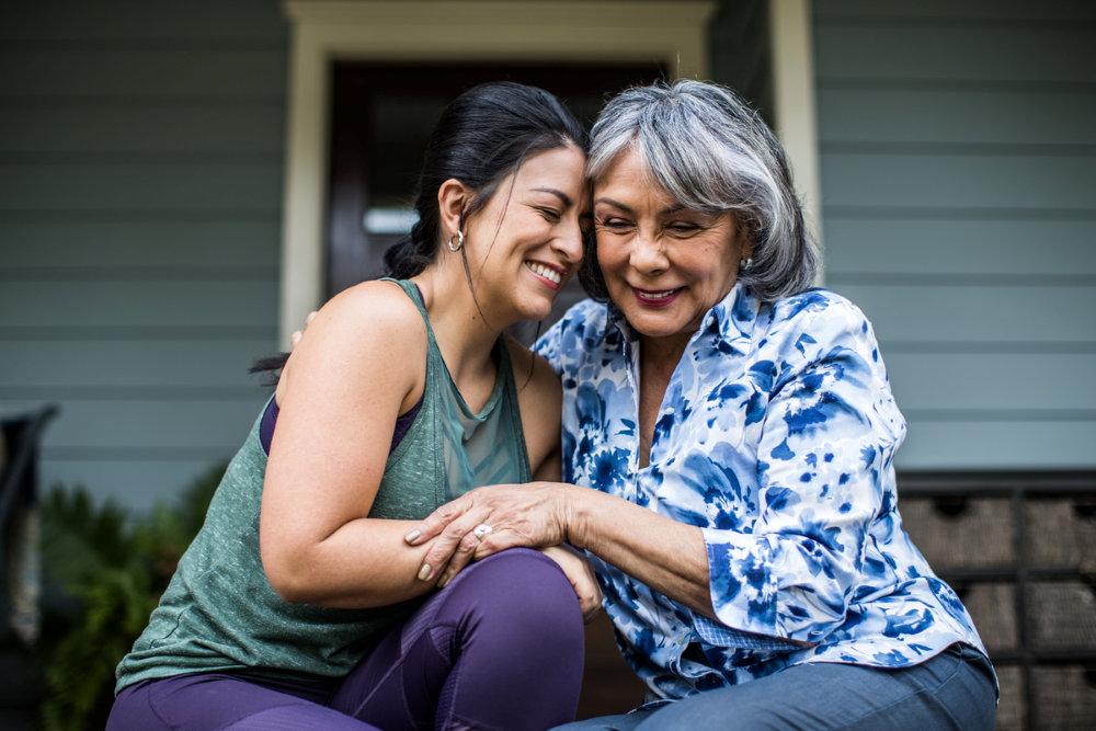 Mother and daughter sitting outside house, laughing and hugging