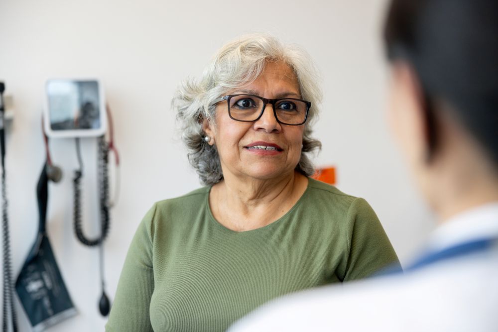 Older woman sitting in doctor's room, talking to health professional