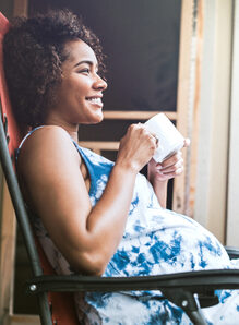 Pregnant person sitting on porch holding a cup