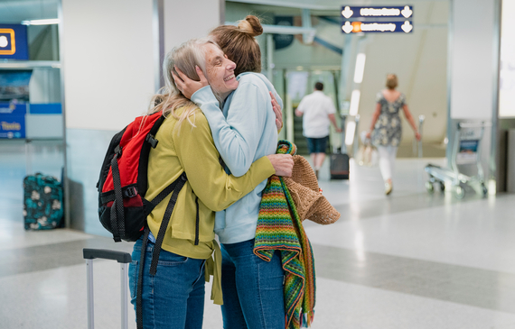 Young woman is giving her mother an emotional cuddle in the airport terminal before she leaves to board a flight.