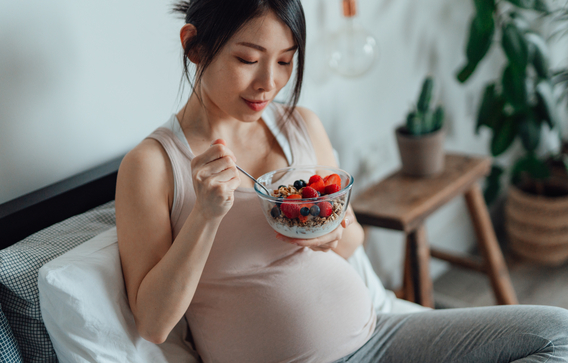 pregnant woman eating a bowl of granola with fruit