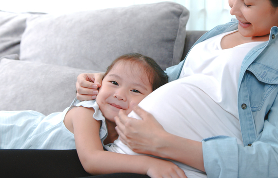 Pregnant mother with child kissing her mums belly.