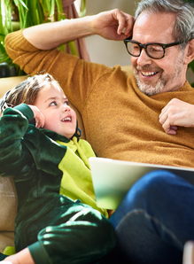 Grandfather sitting with granddaughter having fun while he looks at information on a laptop