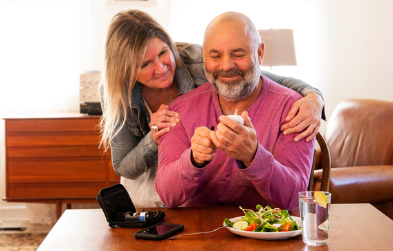 A man checking his blood glucose at home with the support of his partner. 