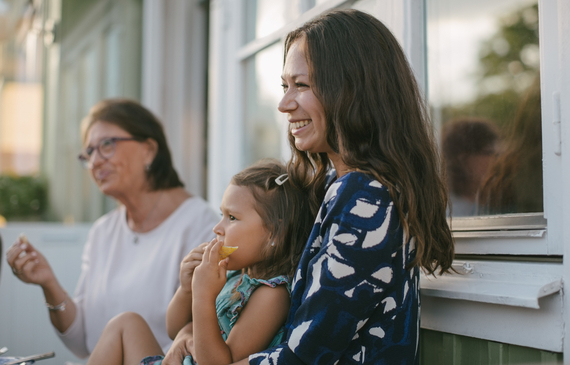 mother with daughter eating fruit while sitting by older woman on verandah