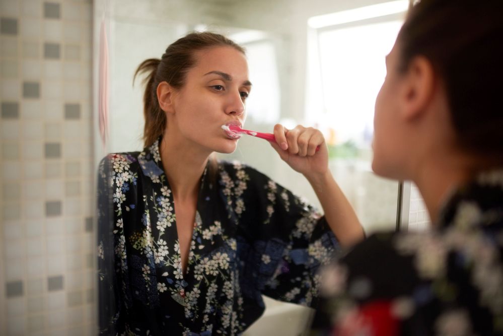 Woman brushing her teeth in the bathroom, looking into mirror