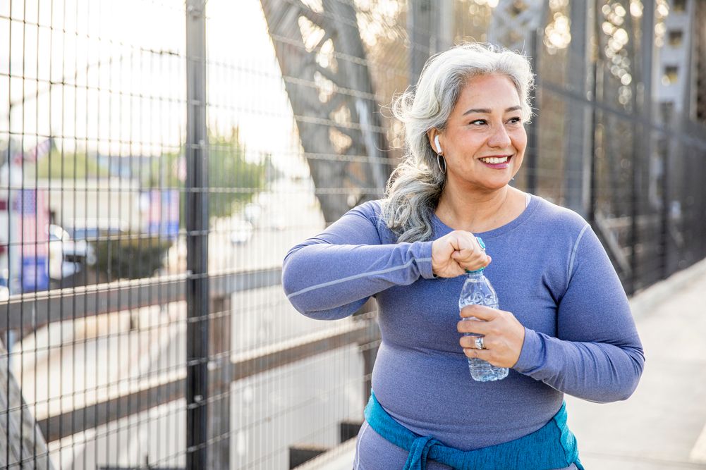 Woman walking on a bridge, stopping to take a drink of water from water bottle