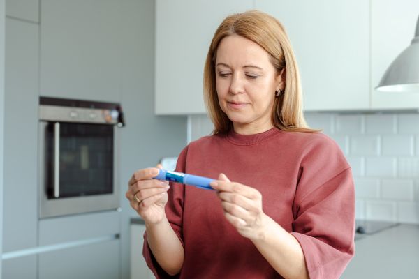 Woman standing in kitchen, looking at insulin pen