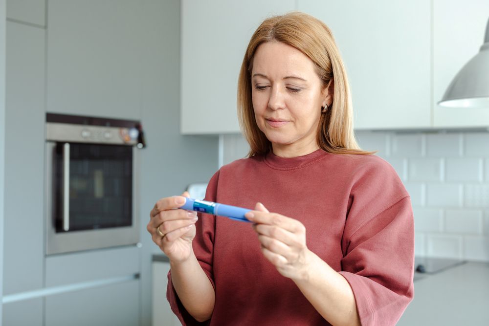 Woman standing in her kitchen, looking at insulin pen