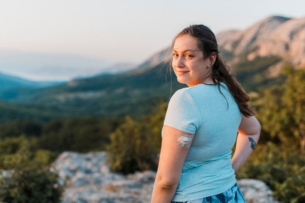 Woman with a cgm device on arm, standing on top of a mountain